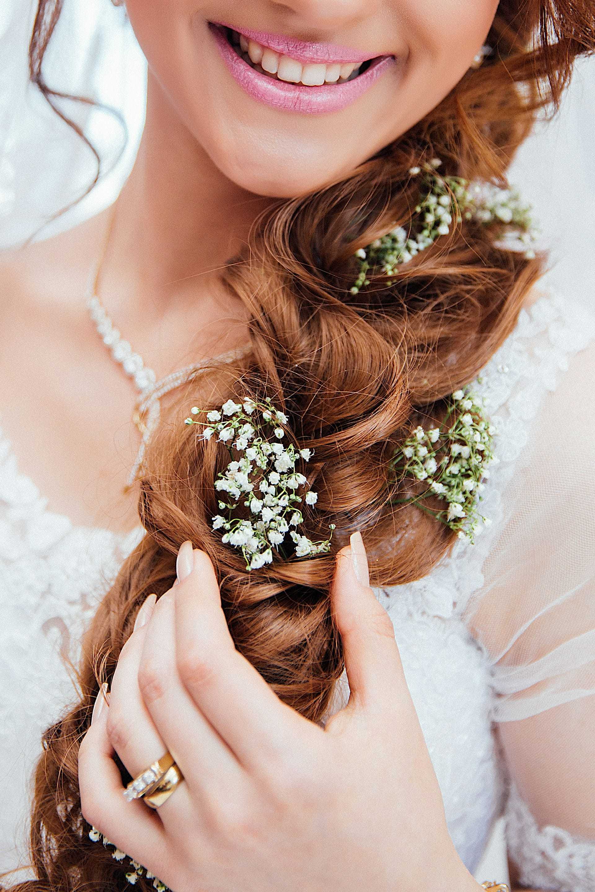Bride with braided hair adorned with white flowers, wearing pearl necklace and wedding dress.