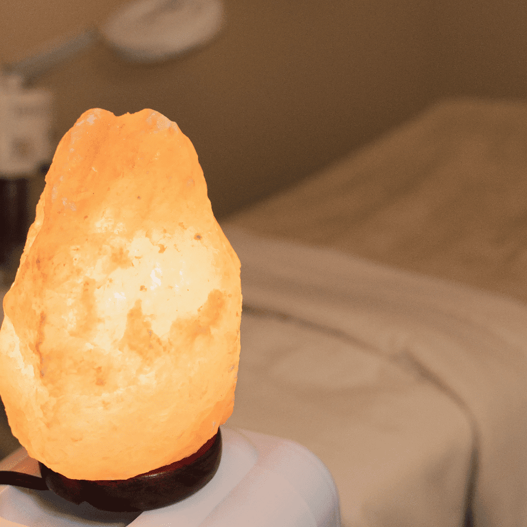 Himalayan salt lamp glowing warmly in a cozy, dimly lit room with a bed in the background.