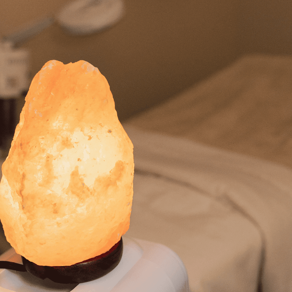 Himalayan salt lamp glowing warmly in a cozy, dimly lit room with a bed in the background.