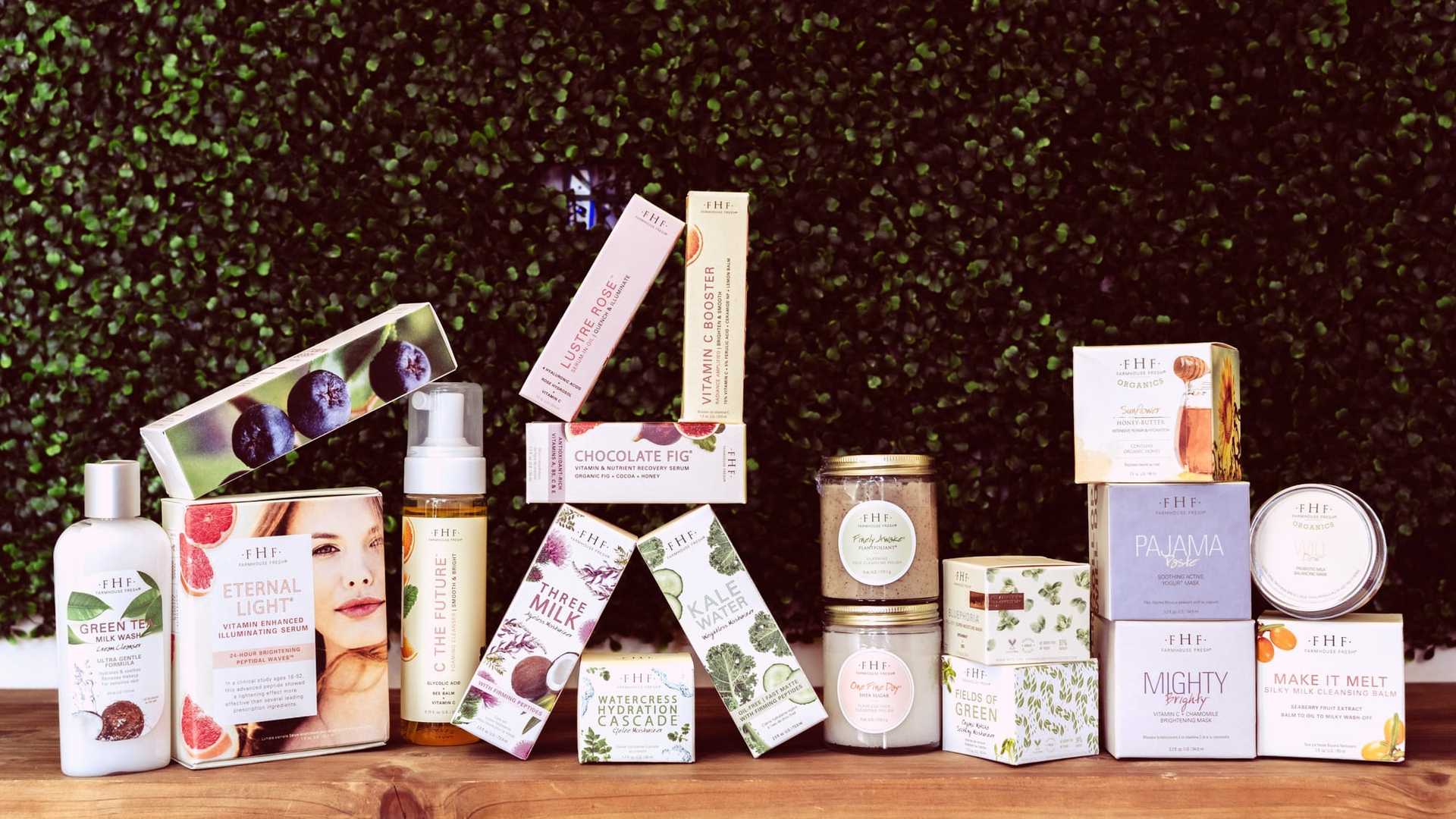Assorted natural skincare products displayed on a wooden table against a green foliage backdrop.